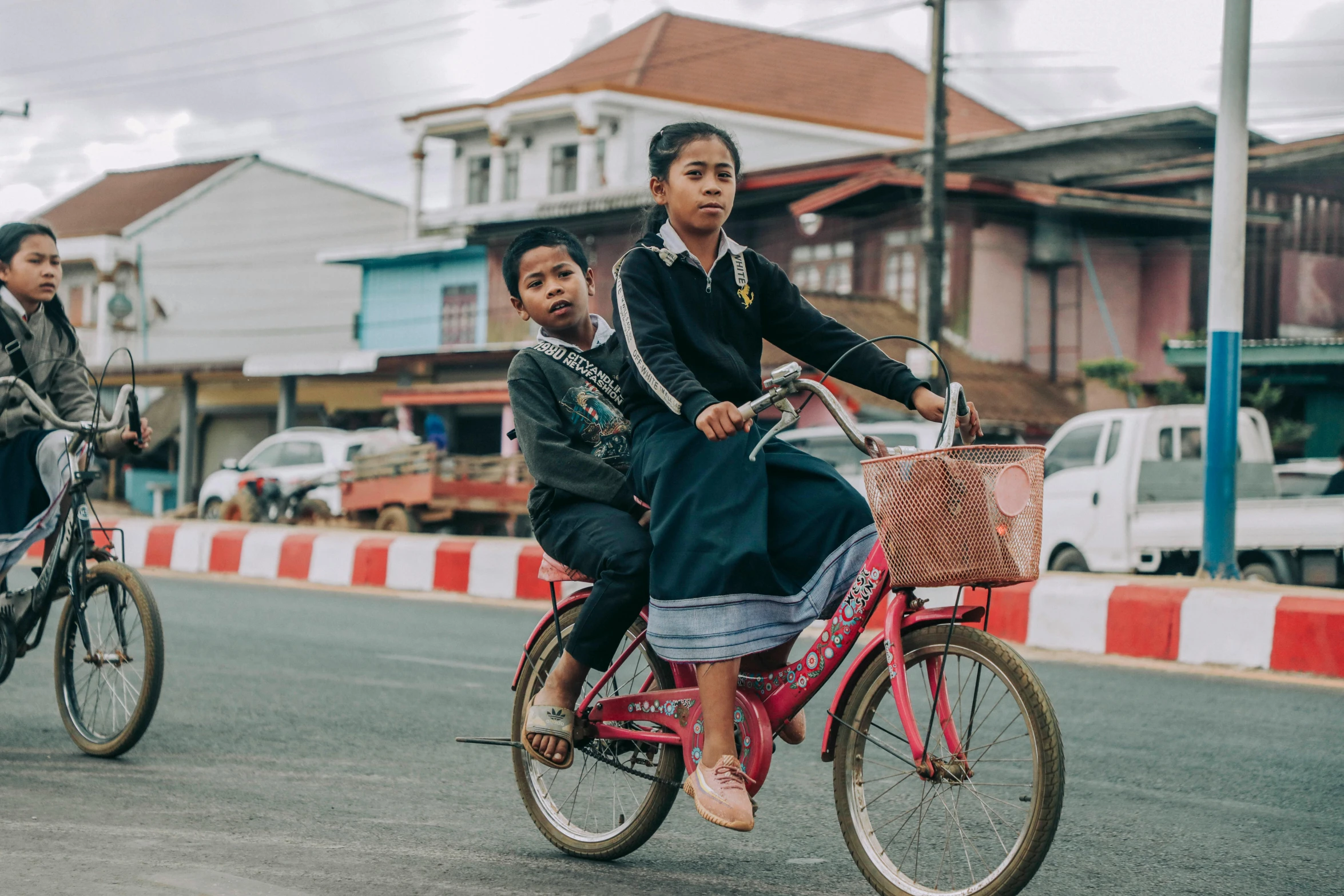 a group of people riding bikes down a street, an album cover, pexels contest winner, sukhothai costume, boy and girl, square, 435456k film