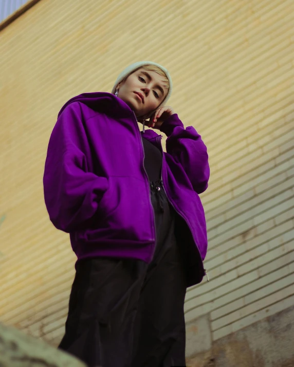 a man in a purple jacket talking on a cell phone, an album cover, inspired by Elsa Bleda, trending on pexels, girl wearing hoodie, nonbinary model, intimidating pose, looking off to the side