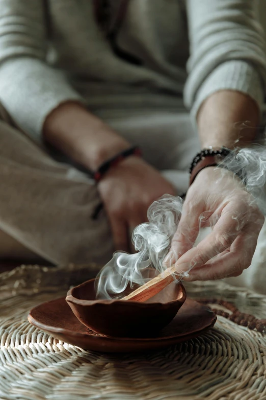 a person sitting in front of a bowl with smoke coming out of it, rituals, sage, promo image, cozy atmosphere