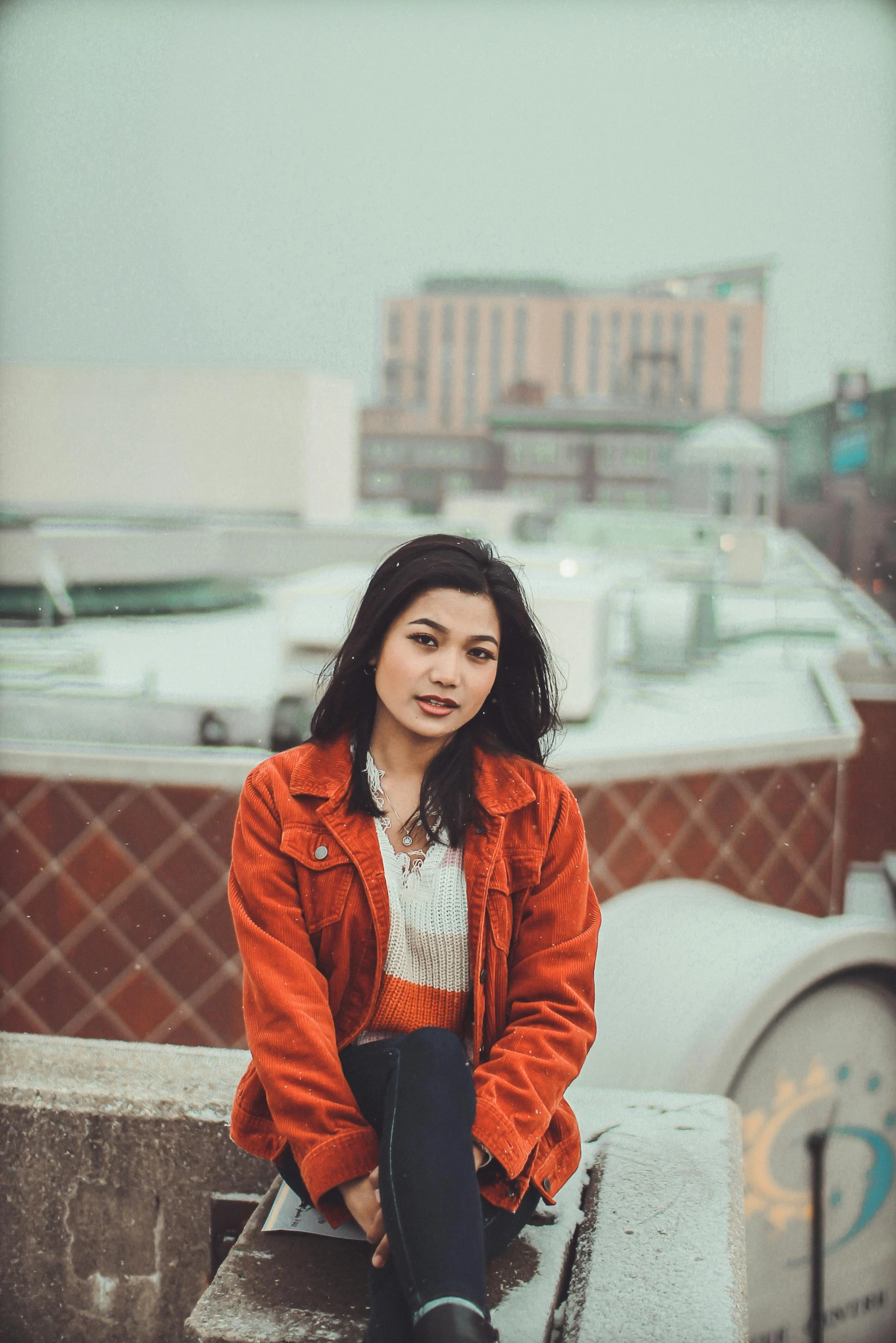 a woman sitting on top of a cement wall, inspired by Elsa Bleda, pexels contest winner, renaissance, orange jacket, asian female, headshot, standing on rooftop