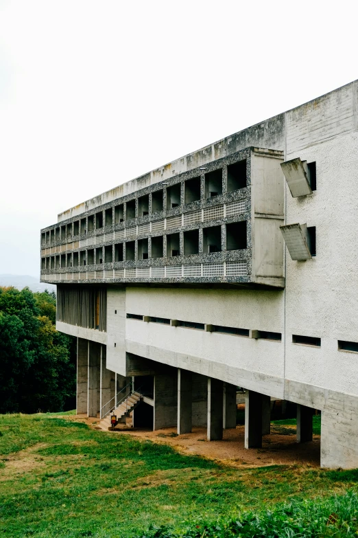 a large concrete building sitting on top of a lush green field, unsplash, brutalism, built on a steep hill, zdzislaw bekinski, balconies, 1981 photograph