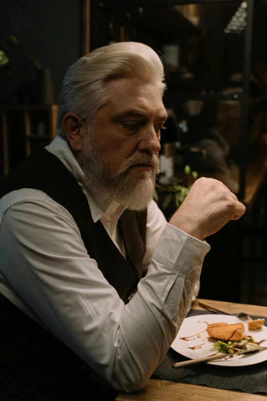 a man sitting at a table with a plate of food, inspired by László Beszédes, reddit, worksafe. cinematic, greybeard, ( ( theatrical ) ), mid shot portrait