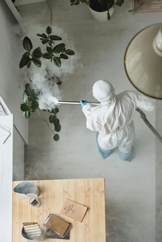 a person in a white suit spraying a plant, leaving a room, wide overhead shot, high particle count, covid