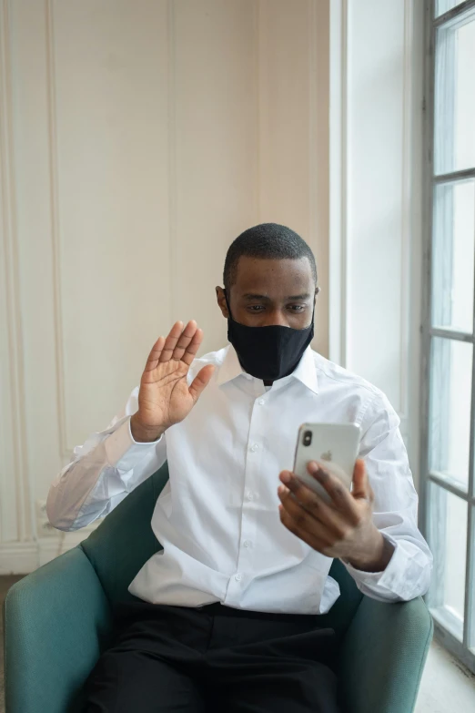 a man sitting in a chair using a cell phone, white man with black fabric mask, greeting hand on head, mkbhd, ignant