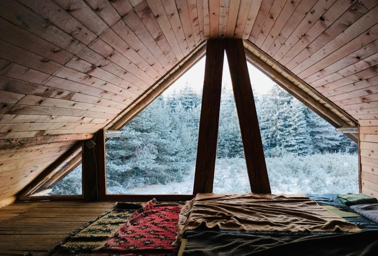 a bed sitting on top of a wooden floor next to a window, by Jessie Algie, unsplash contest winner, fir trees, vaulted ceiling, snowfall, hidden tiny houses