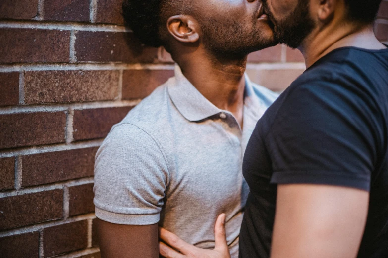 a couple kissing in front of a brick wall, trending on pexels, gay, with brown skin, background image, brightly lit