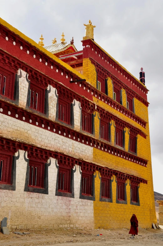 a person walking in front of a yellow and red building, a mosaic, inspired by Yang Buzhi, flickr, in a monestry natural lighting, tibet, up there, square