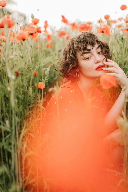a woman sitting in a field of red flowers, inspired by Elsa Bleda, pexels contest winner, color field, side portrait of imogen poots, vibrant orange, natalia dyer, androgynous person