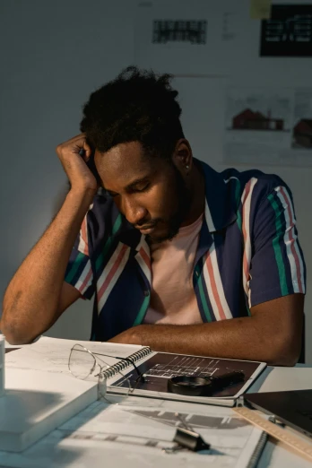 a man sitting at a table in front of a laptop computer, an album cover, trending on unsplash, academic art, tired expression, dark-skinned, architect, embracing
