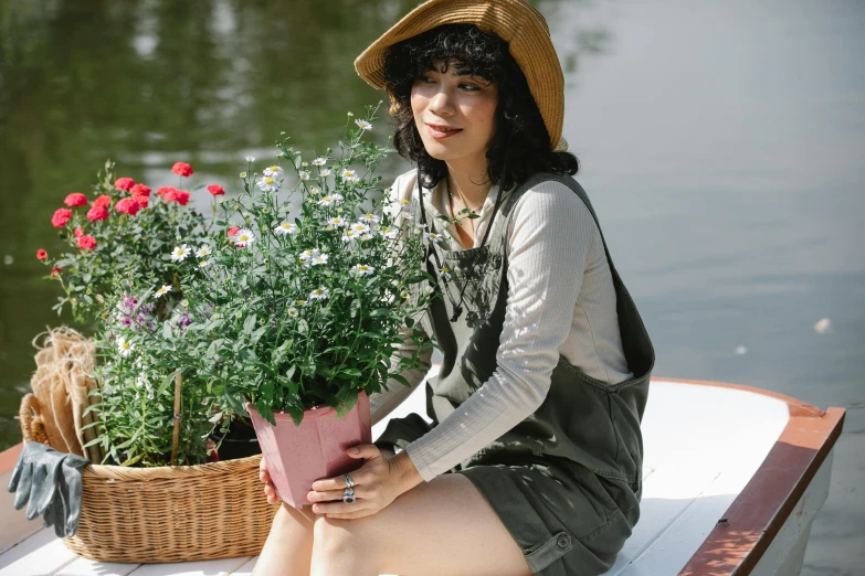 a woman sitting on a boat with a basket of flowers, inspired by Yuko Tatsushima, unsplash, wearing overalls, gardening, press shot, portrait image