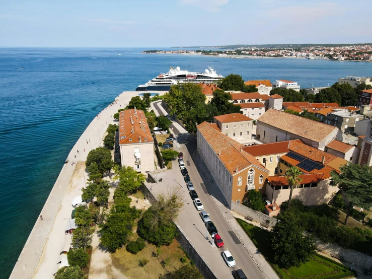 a group of cars driving down a road next to a body of water, by Tom Wänerstrand, pexels contest winner, croatian coastline, white buildings with red roofs, square, 4k panoramic