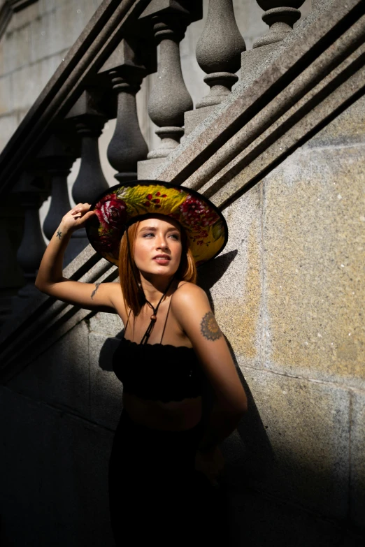 a woman in a hat leaning against a wall, an album cover, inspired by Hedi Xandt, pexels contest winner, wearing sombrero, strong backlight, fashion shoot 8k, square