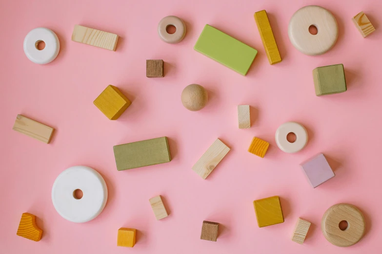 a bunch of wooden toys on a pink surface, inspired by Frederick Hammersley, trending on unsplash, sweets, subtle pattern, spare parts, floating stones