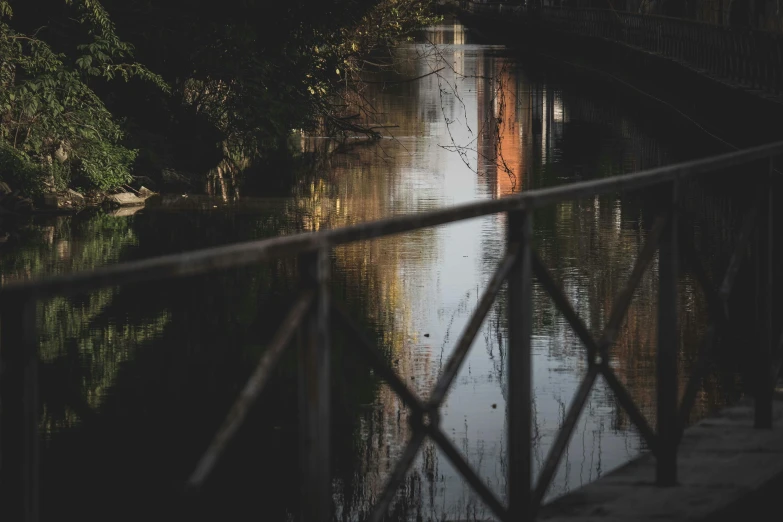 a bridge over a body of water with a building in the background, inspired by Elsa Bleda, pexels contest winner, railing along the canal, harsh shadows and reflections, river in the wood, sewage