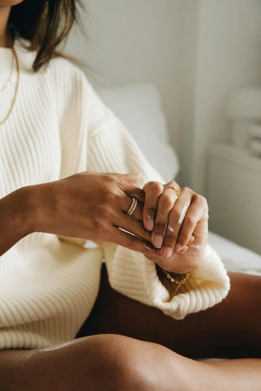 a woman in a white sweater sitting on a bed, inspired by L. A. Ring, trending on pexels, minimalism, wearing two metallic rings, soft evening lighting, layers, sitting in chair