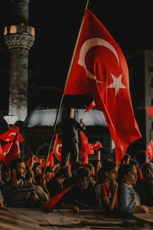 a crowd of people holding flags in front of a building, an album cover, by Nazmi Ziya Güran, pexels, hurufiyya, turkey, square, summer night, thinker