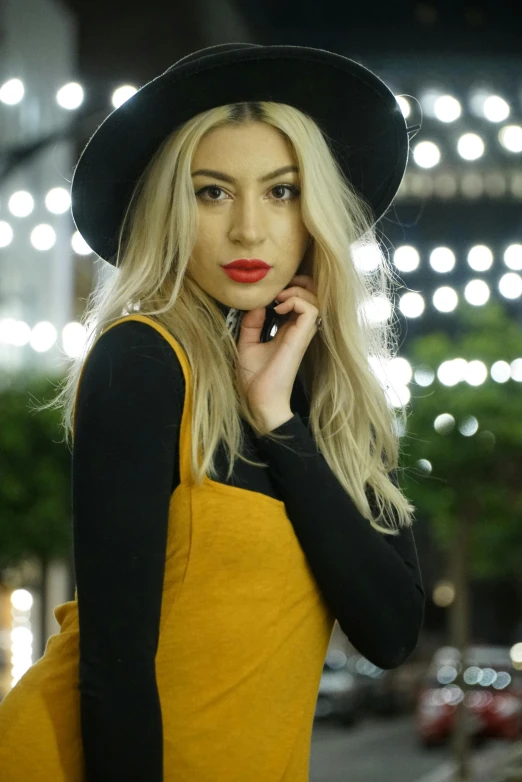 a woman standing on a city street talking on a cell phone, trending on pexels, renaissance, long yellow hair, black hat, katherine mcnamara inspired, yellow overall