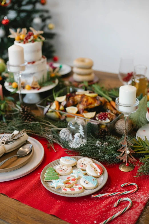 a table topped with plates of food next to a christmas tree, by Julia Pishtar, desserts, dynamic closeup, back towards camera, cast