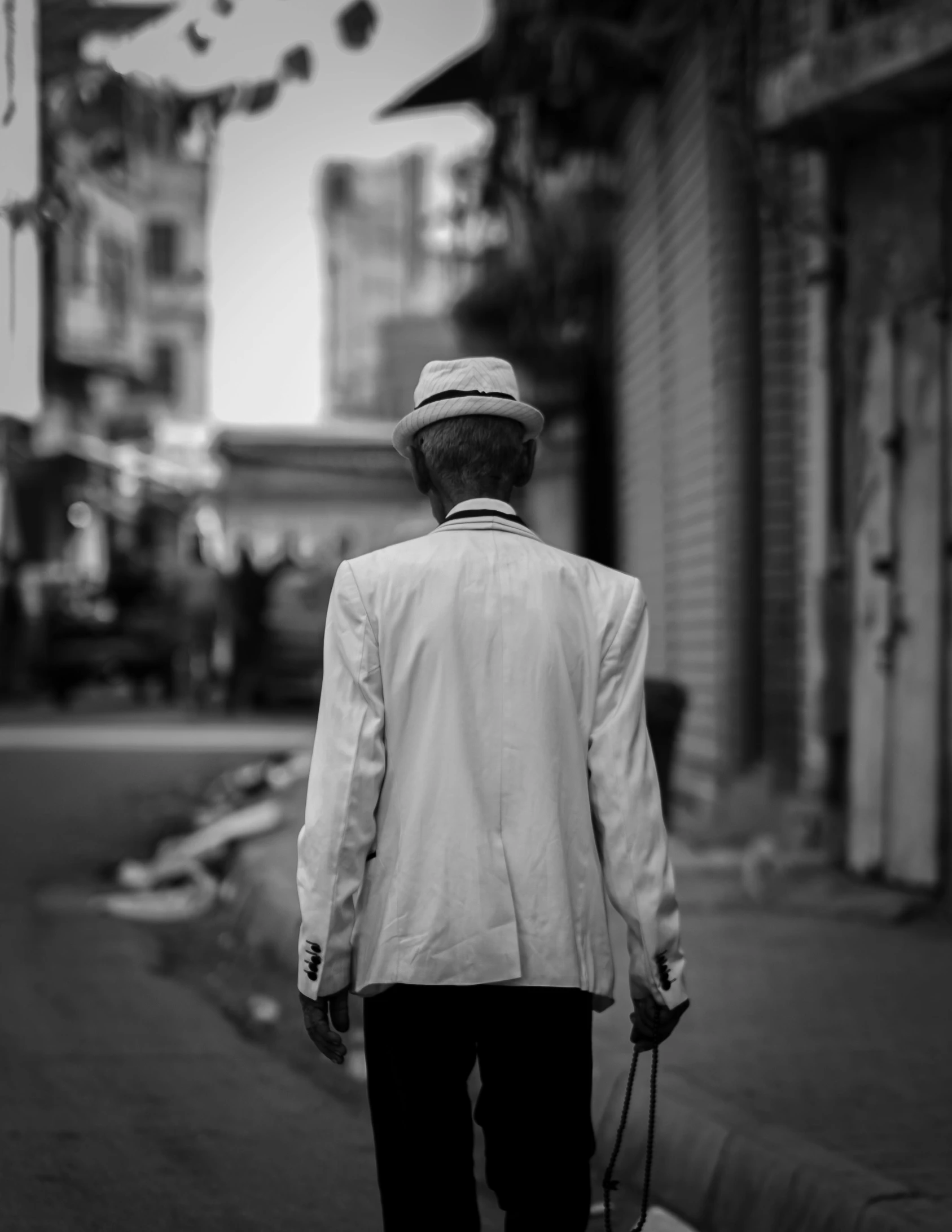 a black and white photo of a man walking down the street, by Youssef Howayek, cinematic. by leng jun, white suit and hat, portrait of an old, back turned