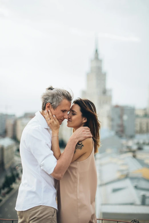 a man and woman standing next to each other on a balcony, a photo, by Adam Marczyński, pexels contest winner, city skyline in the background, gray haired, making out, excited russians