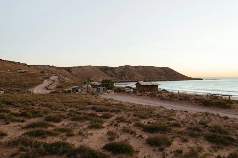 a dirt road next to a body of water, les nabis, sunset beach, small settlements, red sand, exterior shot