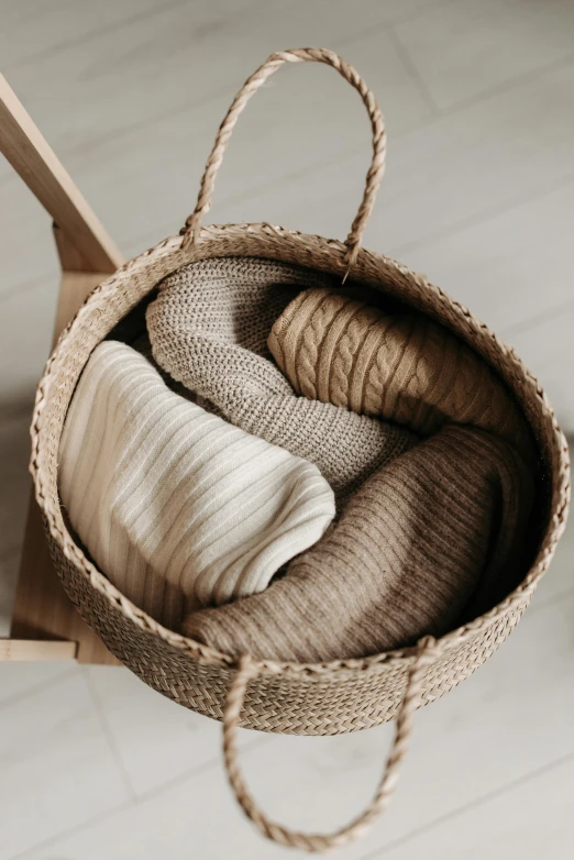 a basket filled with blankets sitting on top of a wooden chair, trending on pexels, renaissance, brown sweater, beige, loaves, taupe