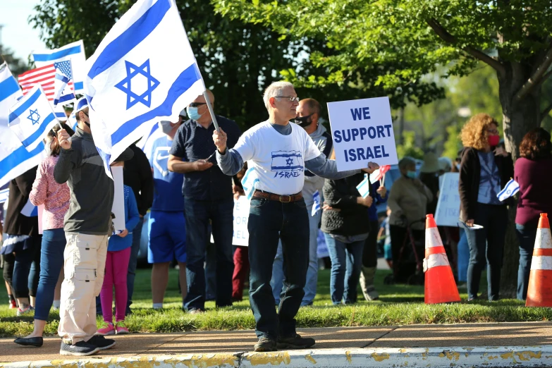 a group of people holding american and israeli flags, a cartoon, a person standing in front of a, support, anthony moravian, detailed zoom photo