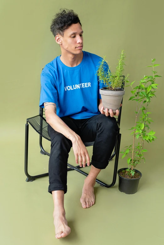 a man sitting in a chair holding a potted plant, blue tight tshirt, ((blue)), sustainable, lookbook