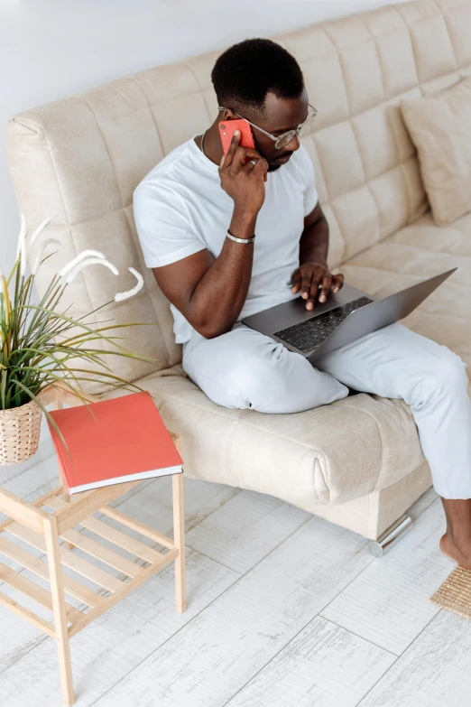 a man sitting on a couch talking on a cell phone, pexels contest winner, laptops, wearing off - white style, african canadian, selling insurance