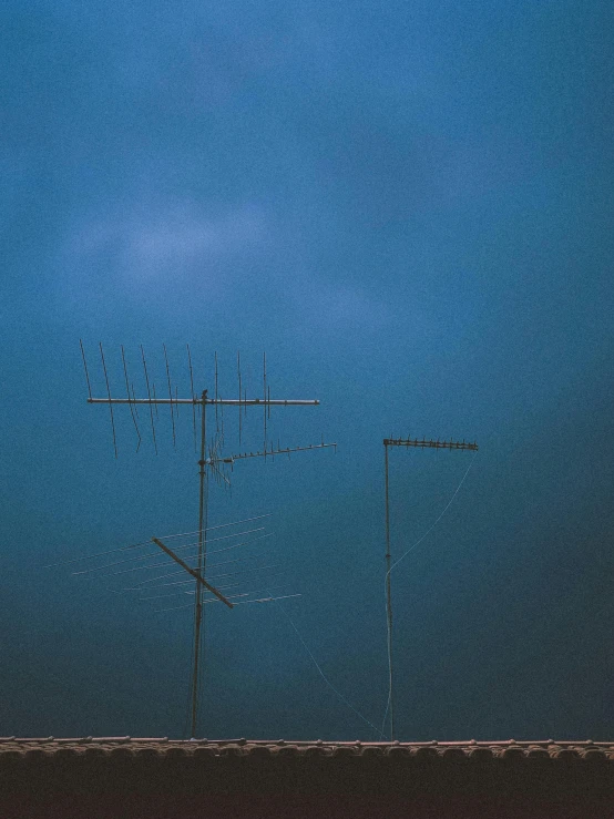 a couple of antennas sitting on top of a roof, an album cover, by Attila Meszlenyi, unsplash, postminimalism, stormy weather at night, ☁🌪🌙👩🏾, 1975, three masts