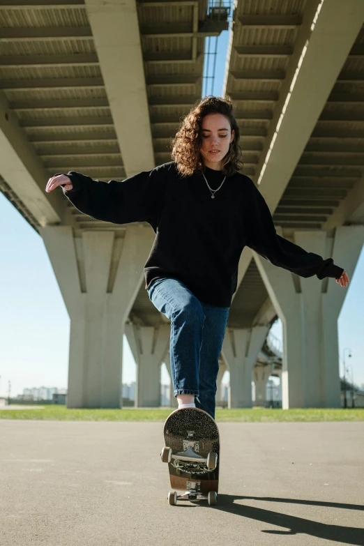 a woman riding a skateboard under a bridge, unsplash contest winner, realism, wearing jeans and a black hoodie, wavy hair spread out, 2000s photo, confident stance