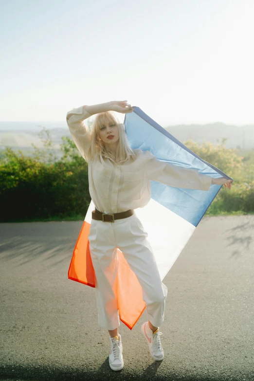 a woman standing in the middle of a road holding a flag, an album cover, inspired by Vincent Lefevre, white bangs, orange and blue, porcelain pale skin, french flag