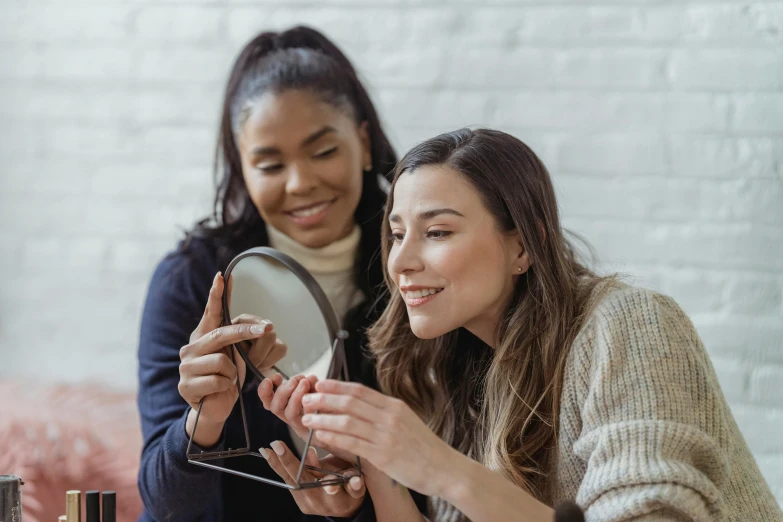 two women sitting at a table in front of a mirror, a photo, trending on pexels, silver monocle, holds a smart phone in one hand, avatar image, beauty shot