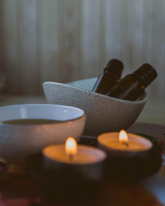 a couple of candles sitting on top of a table, a still life, unsplash, wearing a grey robe, black oil bath, oils, cosy