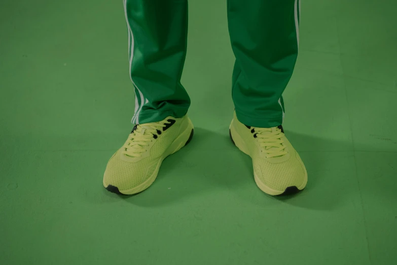 a man standing on top of a green floor next to a tennis racquet, by Attila Meszlenyi, dribble, acid-green sneakers, colors: yellow, chappie in an adidas track suit, aphex twin