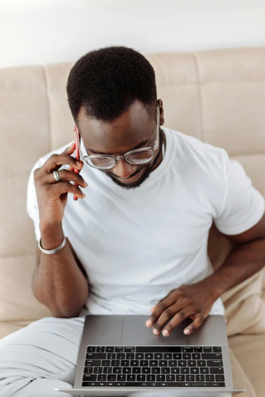 a man sitting on a couch using a laptop computer, trending on pexels, man is with black skin, man with glasses, call now, all white