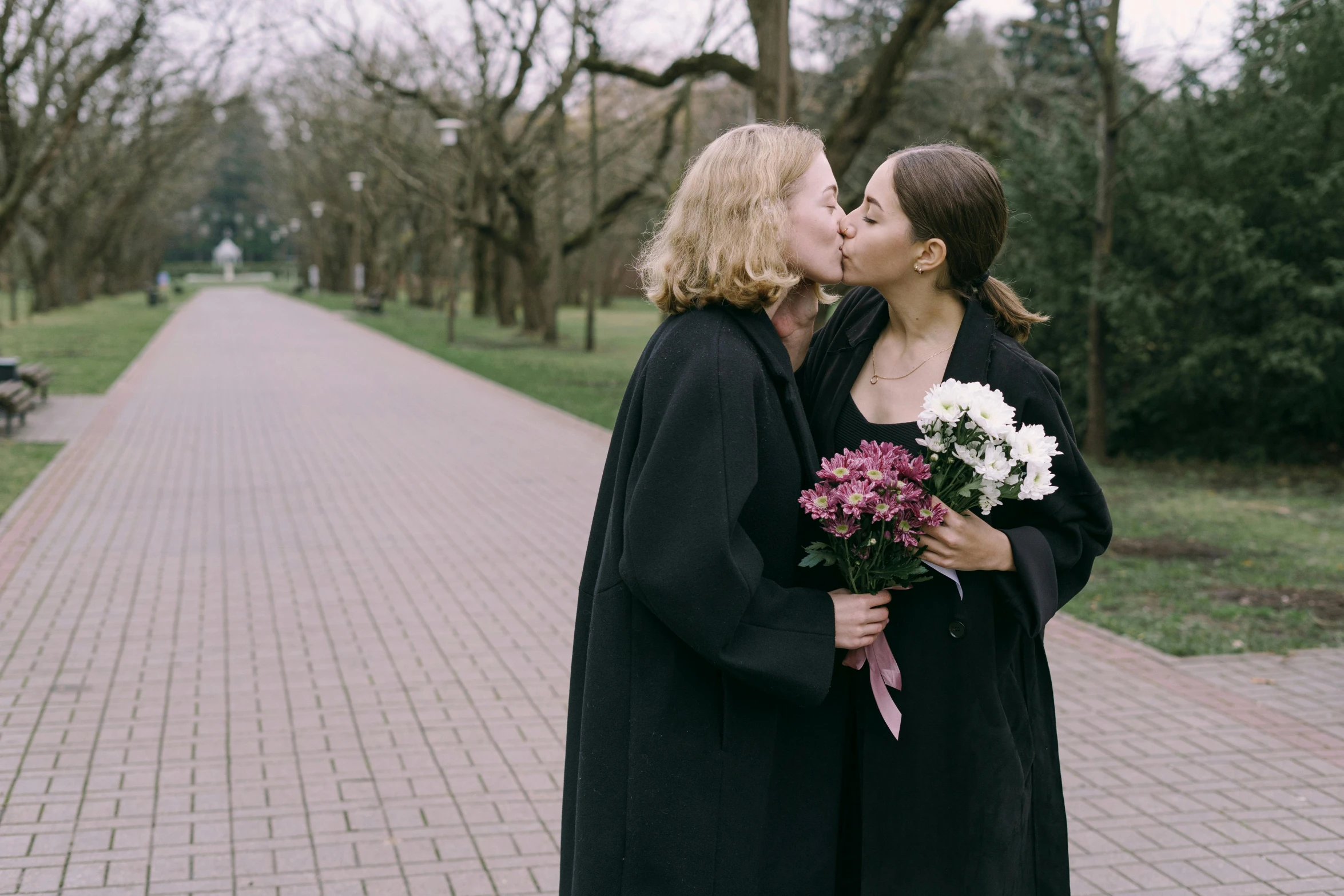 a couple of women standing next to each other, unsplash, romanticism, wearing black robe, bouquet, lesbian kiss, university