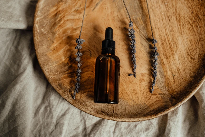 a bottle of essential oil sitting on top of a wooden plate, trending on pexels, arched back, botanicals, lavender, handcrafted