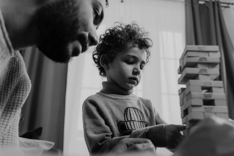 a black and white photo of a man playing with a child, a black and white photo, pexels contest winner, visual art, building blocks, curls on top, thoughtful, four years old