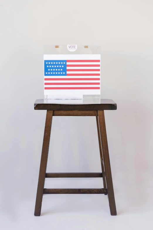 a wooden stool with an american flag painted on it, by Will Ellis, inside its box, the handbag is over a wood table, white space in middle, the white house