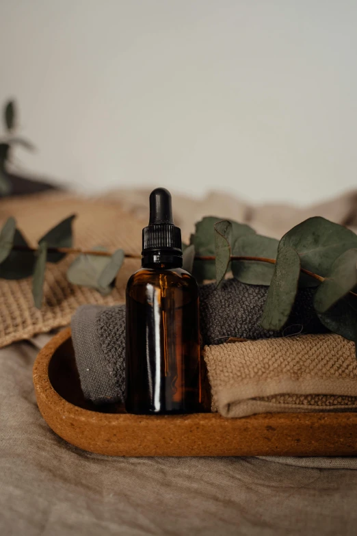 a bottle of essential oil next to a pile of towels, a still life, inspired by Eden Box, unsplash, renaissance, eucalyptus, thumbnail, brown, textured canvas