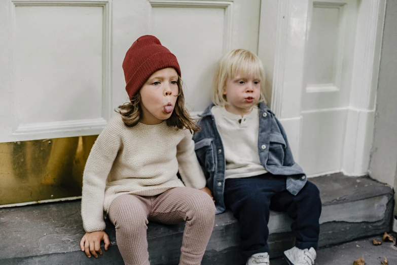 two young children sitting on the steps of a house, by Nina Hamnett, pexels, sweater, maroon hat, a pair of ribbed, mini model