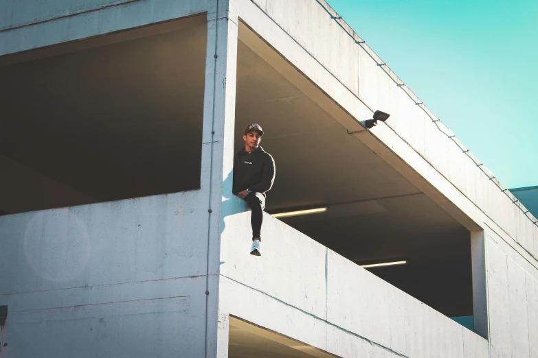 a man sitting on the ledge of a building, liam brazier, outside in parking lot, high quality upload, multiple stories