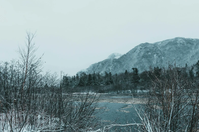 a body of water surrounded by snow covered trees, inspired by Elsa Bleda, unsplash contest winner, hills in the background, gloomy mood, music video, hunting