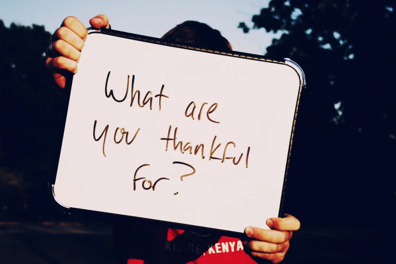 a person holding a sign that says what are you thankful for?, a photo, hurufiyya, avatar image, colour photograph, instagram art, background image