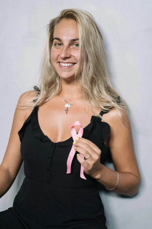 a woman in a black dress holding a pink ribbon, tanned, smiling down from above, taken in the early 2020s, lucas graziano