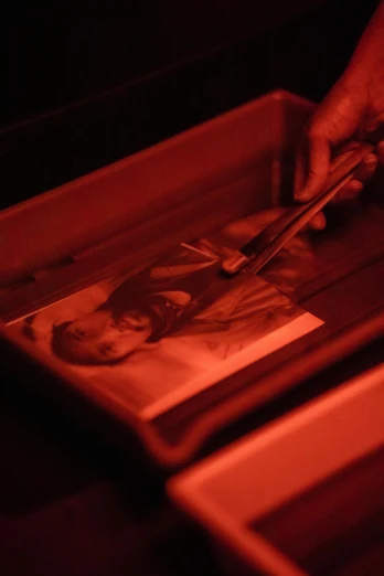a person cutting a picture in a box, an etching, inspired by Carrie Mae Weems, unsplash, holography, red glow, high angle close up shot, glowing powder, gelatin silver finish