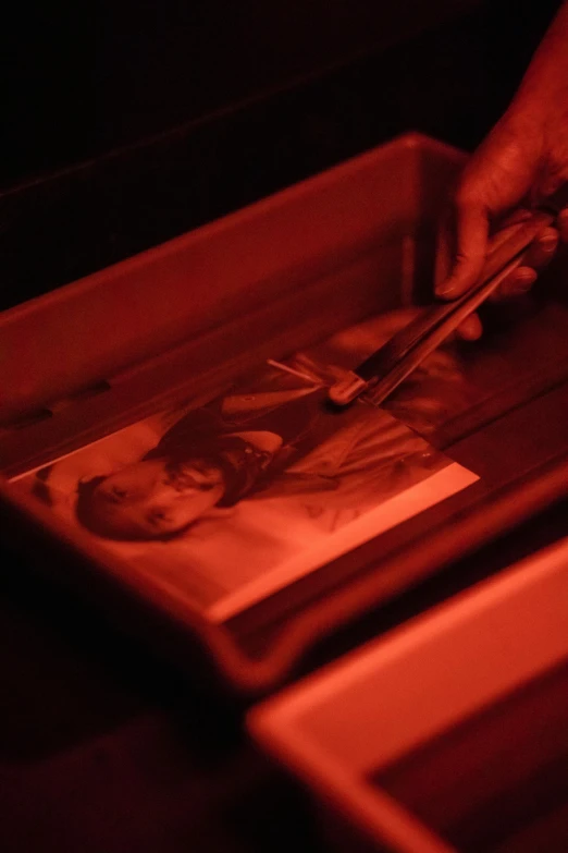 a person cutting a picture in a box, an etching, inspired by Carrie Mae Weems, unsplash, holography, red glow, high angle close up shot, glowing powder, gelatin silver finish