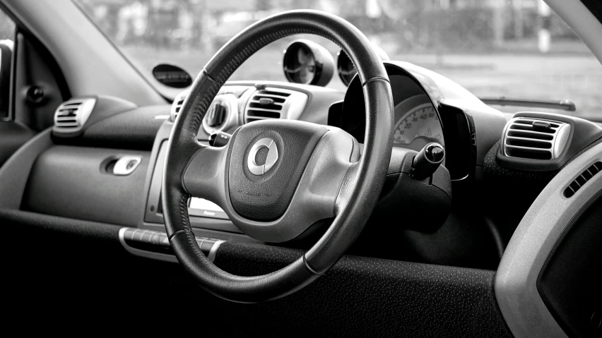 a close up of a steering wheel in a car, a black and white photo, by David Donaldson, pexels, square, mclaren, smart looking, interior of a small