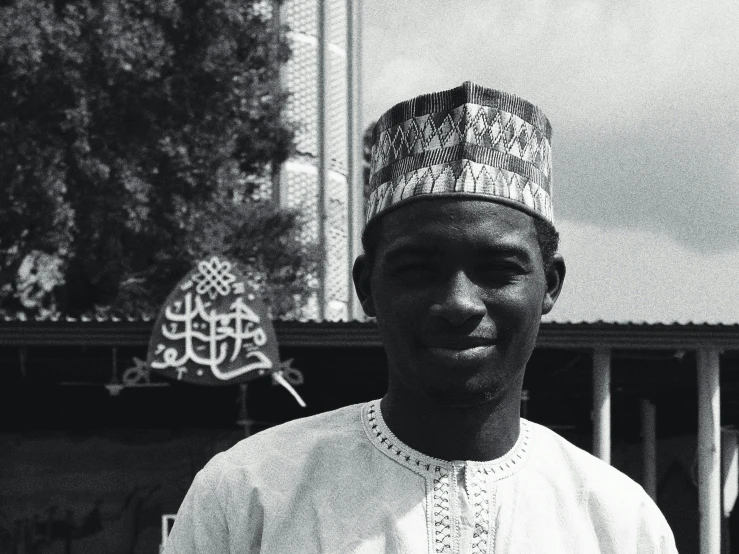 a black and white photo of a man wearing a hat, a black and white photo, hurufiyya, adebanji alade, mosque, he is about 20 years old | short, photo taken on fujifilm superia
